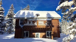 A wooden cabin with a balcony, surrounded by snow-covered trees.