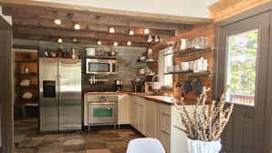 A modern kitchen with a stainless steel refrigerator, a built-in oven, and a microwave. There is a wooden countertop and a dining table with a vase of pinecones.