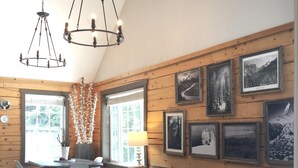 A cozy living room with a black leather sofa, a wooden dining table, and a chandelier.