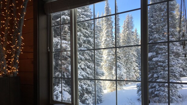 A room with a large window offering a view of snow-covered trees and a clear sky.