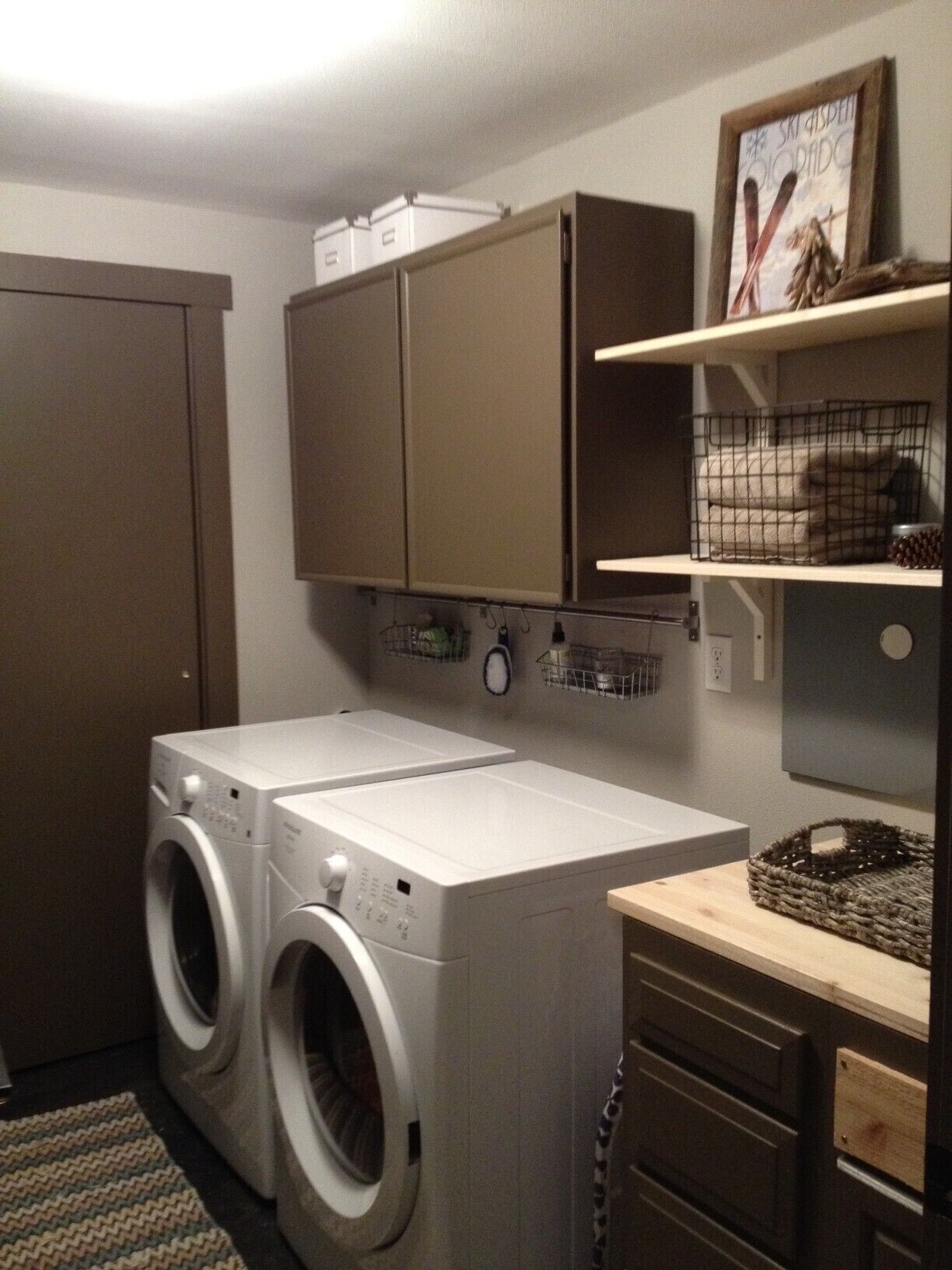 A laundry room with two front-loading washing machines, wooden cabinets, and a shelf with a picture frame.