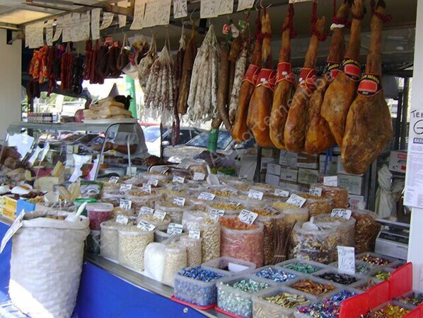 Puesto de mercado con diversos embutidos y aperitivos expuestos en recipientes y colgando.