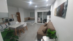 Un salon moderne comprenant un canapé, une table à manger avec des chaises, un coin cuisine avec une cuisinière et une porte-fenêtre coulissante donnant sur un balcon.