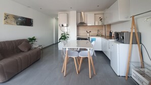 Une cuisine moderne avec des meubles blancs, une table à manger avec des chaises et un canapé dans l’espace salon.