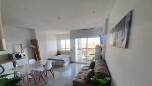 Un salon moderne avec un canapé, une table à manger, des chaises et un petit balcon.