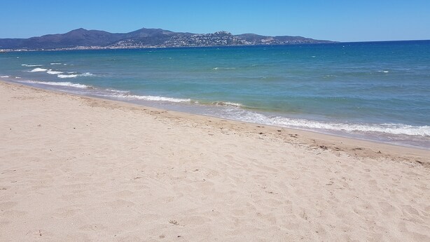 Une plage avec une eau d’un bleu limpide et une montagne en arrière-plan.