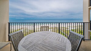 Une terrasse en bois avec une table et des chaises, donnant sur une plage et agrémentée d’une rambarde.