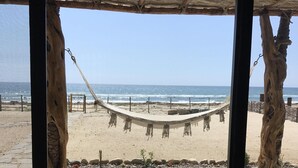 A beach view from a covered area with a hammock and wooden pillars.