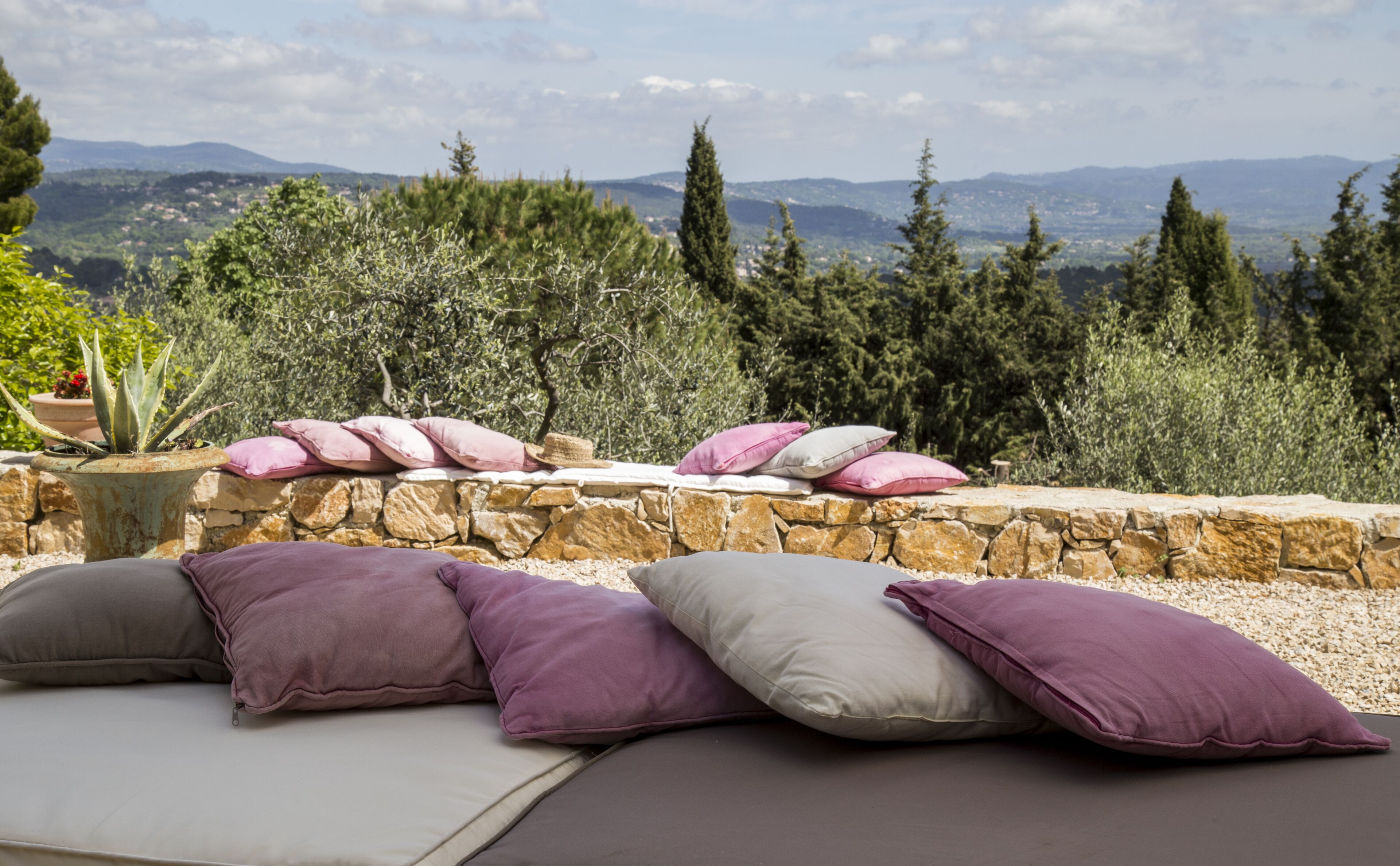 A stone wall with a row of cushions and a potted plant.