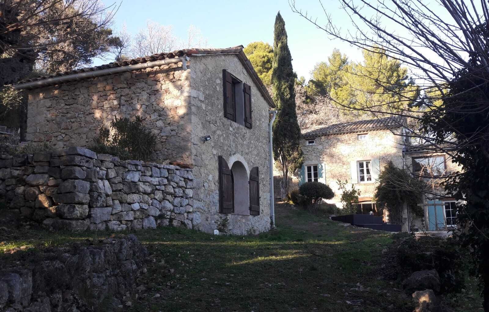 A stone building with a sloped roof, a stone wall, and a small garden area.