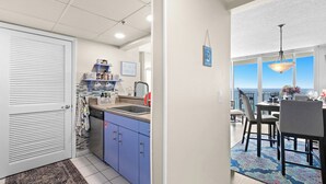 A kitchen with blue cabinets, a sink, and a countertop. There is a dining area with a table and chairs, and a view of the ocean through large windows. - New 1bd w/ OPEN DATES! Sleeps 4 (Panama City Beach)