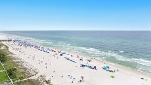 Ein Strand mit Reihen von Sonnenschirmen und Liegestühlen, ein Steg im Hintergrund und der Ozean.