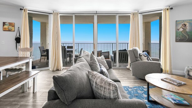 Ein modernes Wohnzimmer mit einem großen grauen Sofa, einem Holztisch und Blick auf den Ozean.
