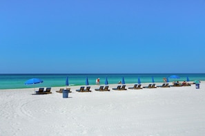 A beach with rows of sun loungers and blue umbrellas, a clear sky, and the ocean in the background. - New 1bd w/ OPEN DATES! Sleeps 4 (Panama City Beach)
