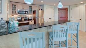 A modern kitchen with stainless steel appliances, a granite countertop, and light blue chairs. - Bayside Resort ~ Large Balcony ~ Family Friendly (Miramar Beach)