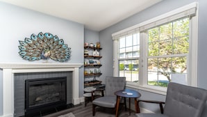 A living room with a fireplace, a peacock wall art, a bookshelf, and a window with a view of the outside. - Lake Chelan Vacation Rental with private pool and hot tub, sleeps up to 12 (Chelan)