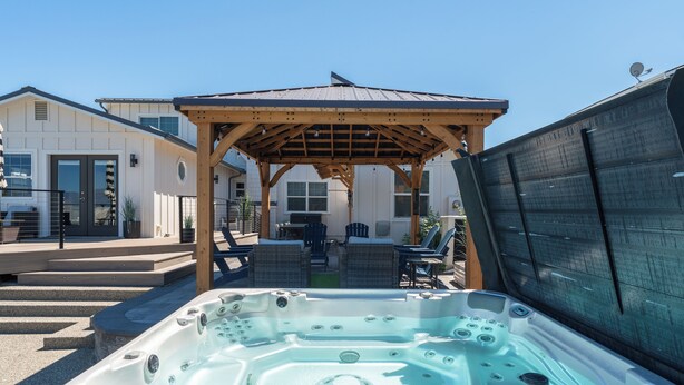 A hot tub with a wooden pergola, outdoor seating, and a house in the background. - Lake Chelan Vacation Rental with private pool and hot tub, sleeps up to 12 (Chelan)