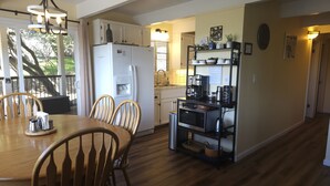 A compact kitchen with a dining area, wooden chairs, a white refrigerator, a coffee machine, and a small shelf with kitchenware. - Woodsy Hideaway~Yosemite views, your getaway starts here, it's a Guest Favorite! (Groveland)