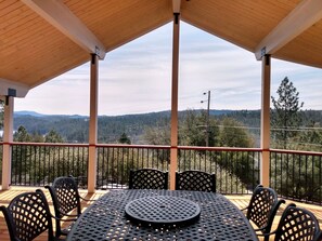 Une terrasse extérieure couverte, dotée d’une table et de chaises, qui offre une vue sur un paysage boisé et des montagnes.