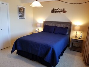 Un lit bien fait, recouvert d’une couvre-lit bleu foncé, avec deux lampes de chevet, un tableau encadré accroché au mur et un élément décoratif fixé au mur au-dessus du lit.