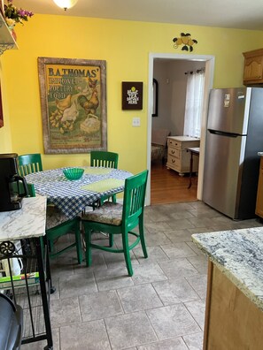 A kitchen with a dining table, chairs, a refrigerator, and a wall with a poster.