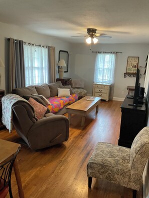 A living room with a sofa, armchairs, a wooden coffee table, a ceiling fan, and a television.