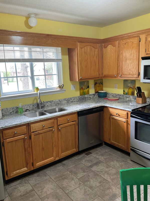 A kitchen with wooden cabinets, a dishwasher, a stove, and a window with blinds.