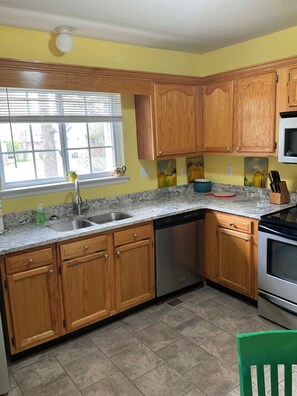 A kitchen with wooden cabinets, a dishwasher, a stove, and a window with blinds.
