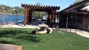 A wooden pergola with a picnic table in a park area by a body of water.
