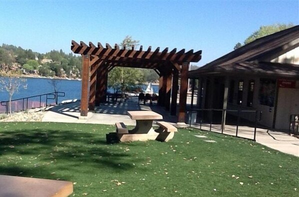 A wooden pergola with a picnic table in a park area by a body of water.