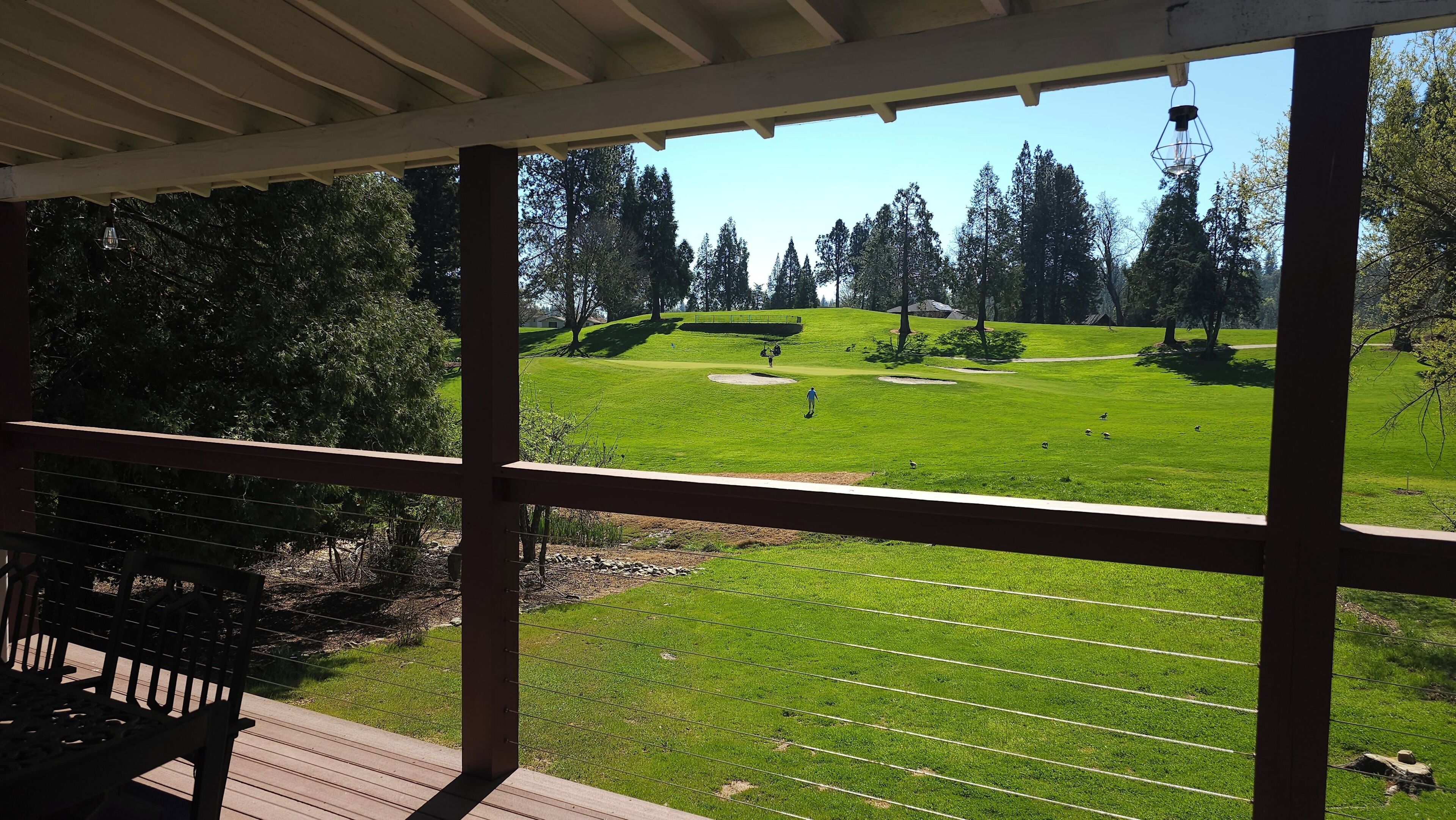 Uitzicht vanaf een overdekt terras op een golfbaan, met een houten terras en een bank.
