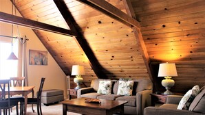 A cozy loft-style room with a sloped ceiling, wooden beams, a sofa set, a coffee table, and two lamps.