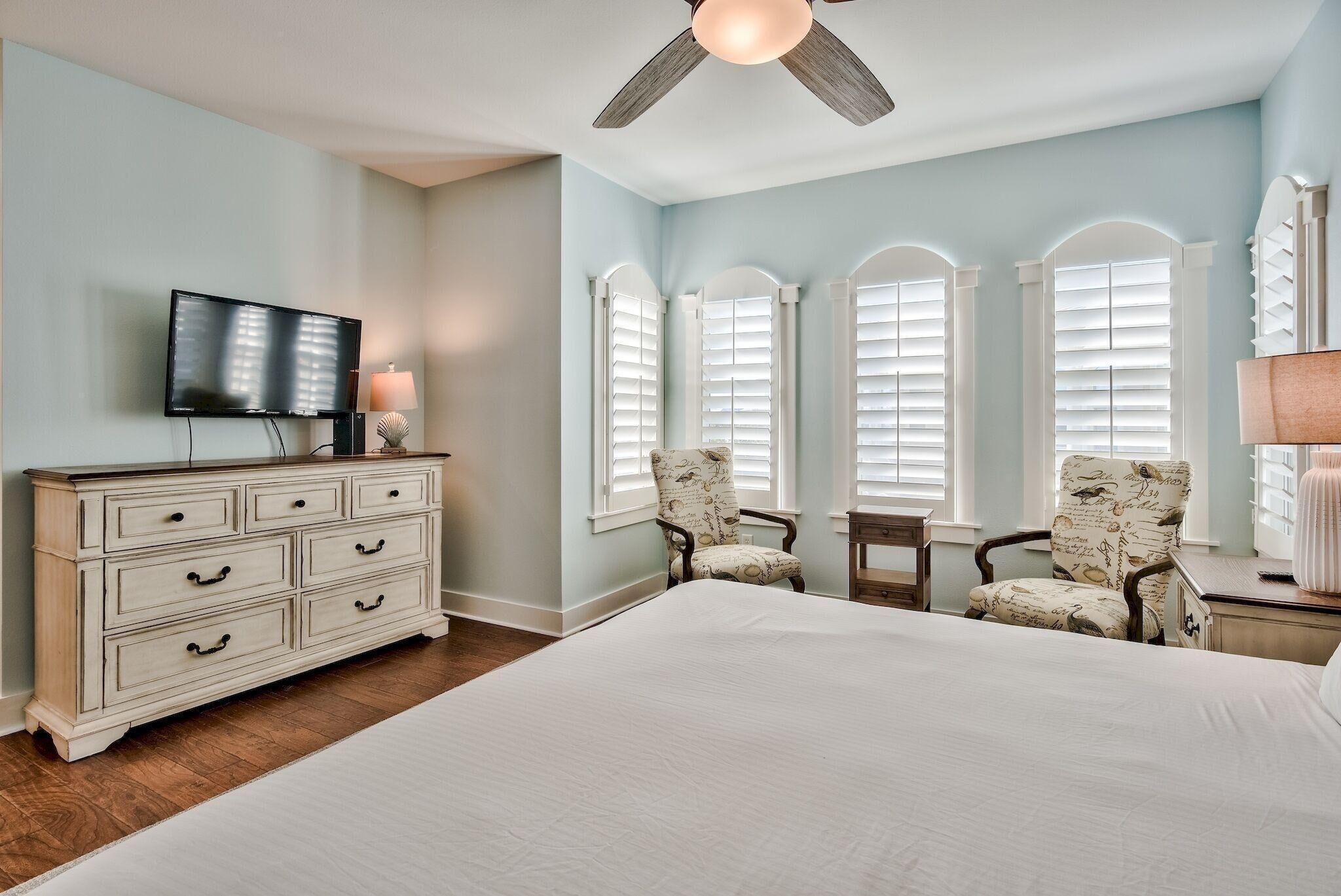 A bedroom with a large bed, a dresser, a television, and a ceiling fan.