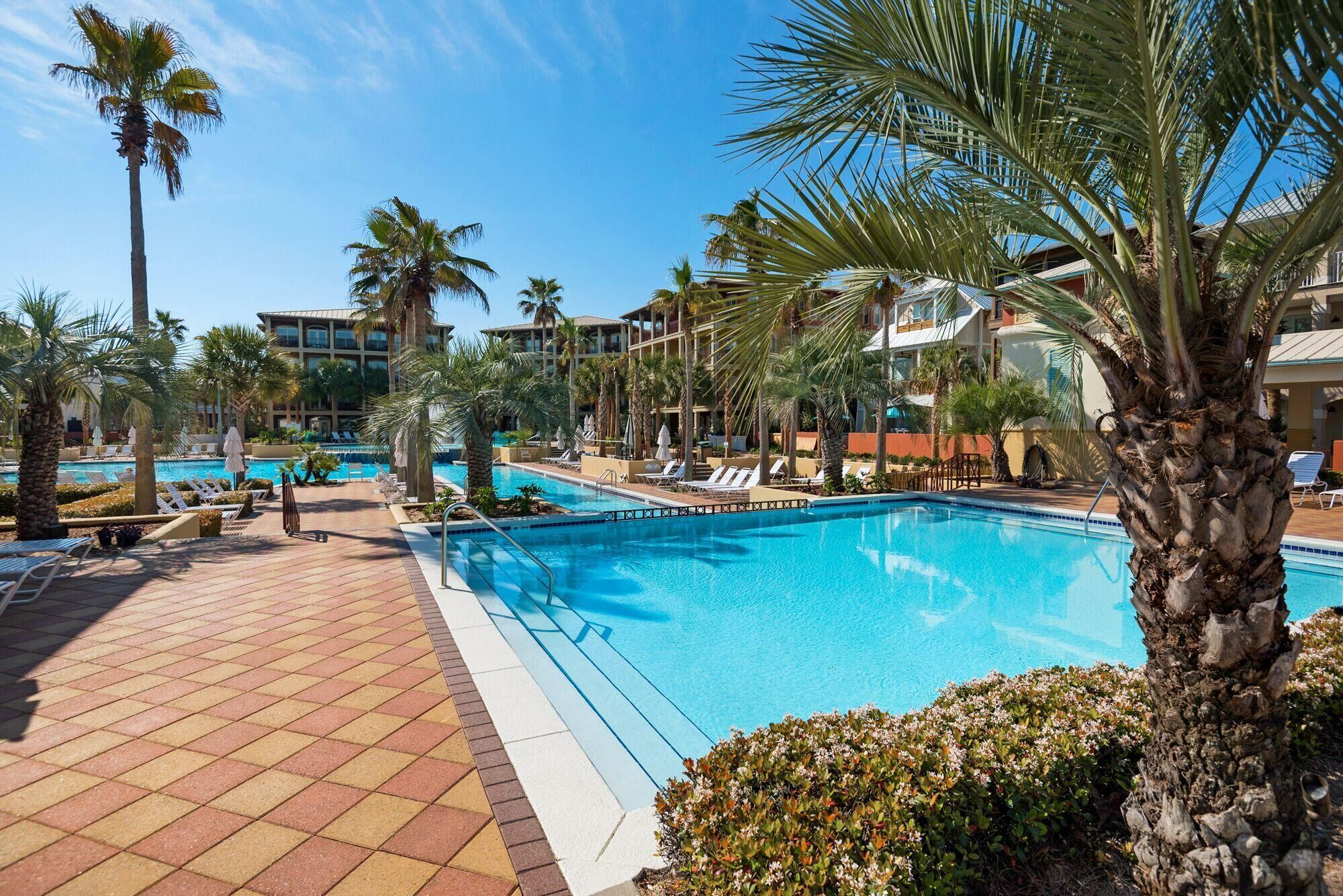 Un espace piscine d’hôtel comprenant plusieurs piscines, des palmiers et des chaises longues.