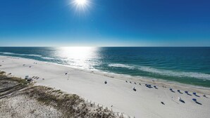 A beach with white sand, clear blue water, and a bright sun in the sky.