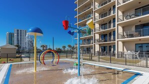 A water play area with a pool, surrounded by a fence, and a multi-story building in the background.