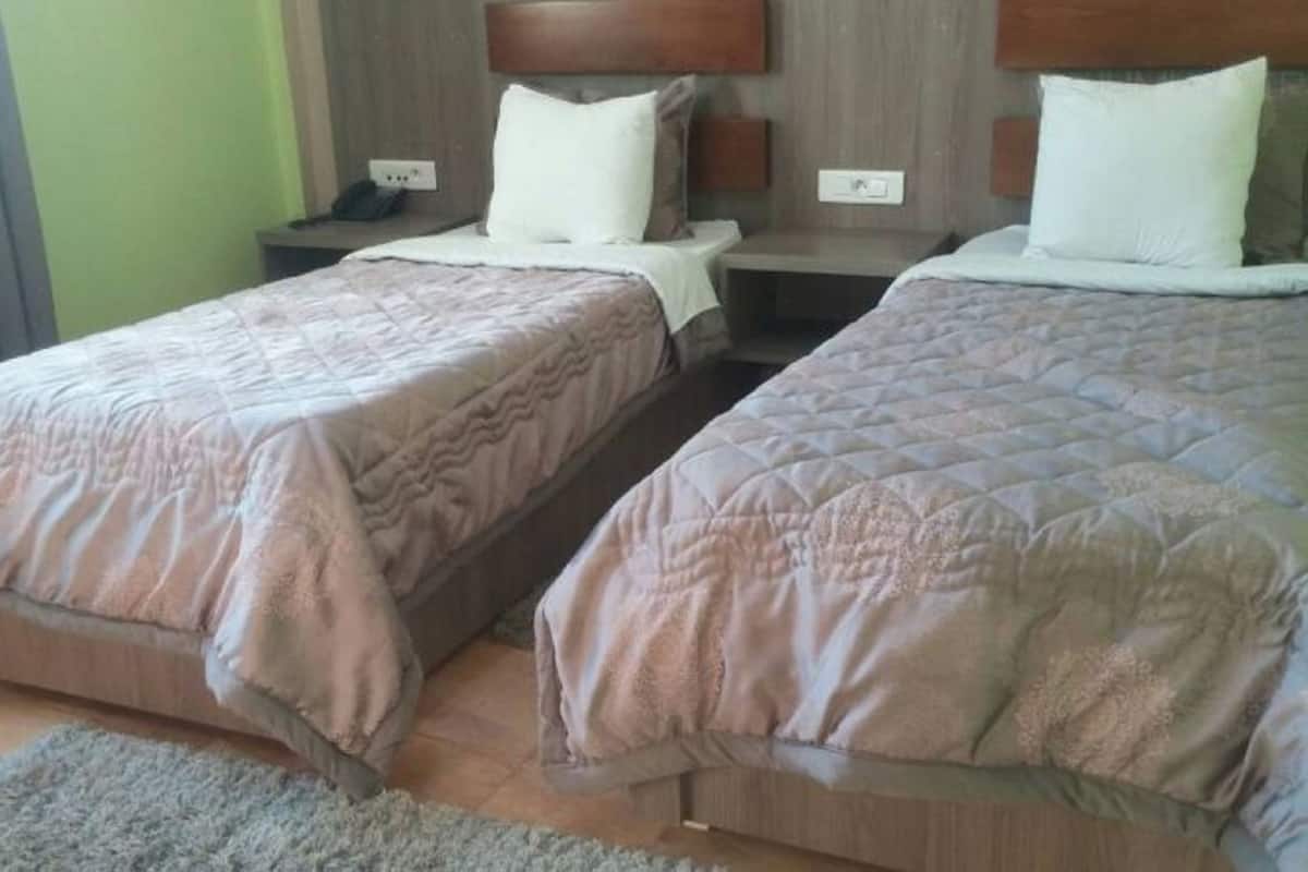 A hotel room with two single beds, each with a wooden headboard and a nightstand.