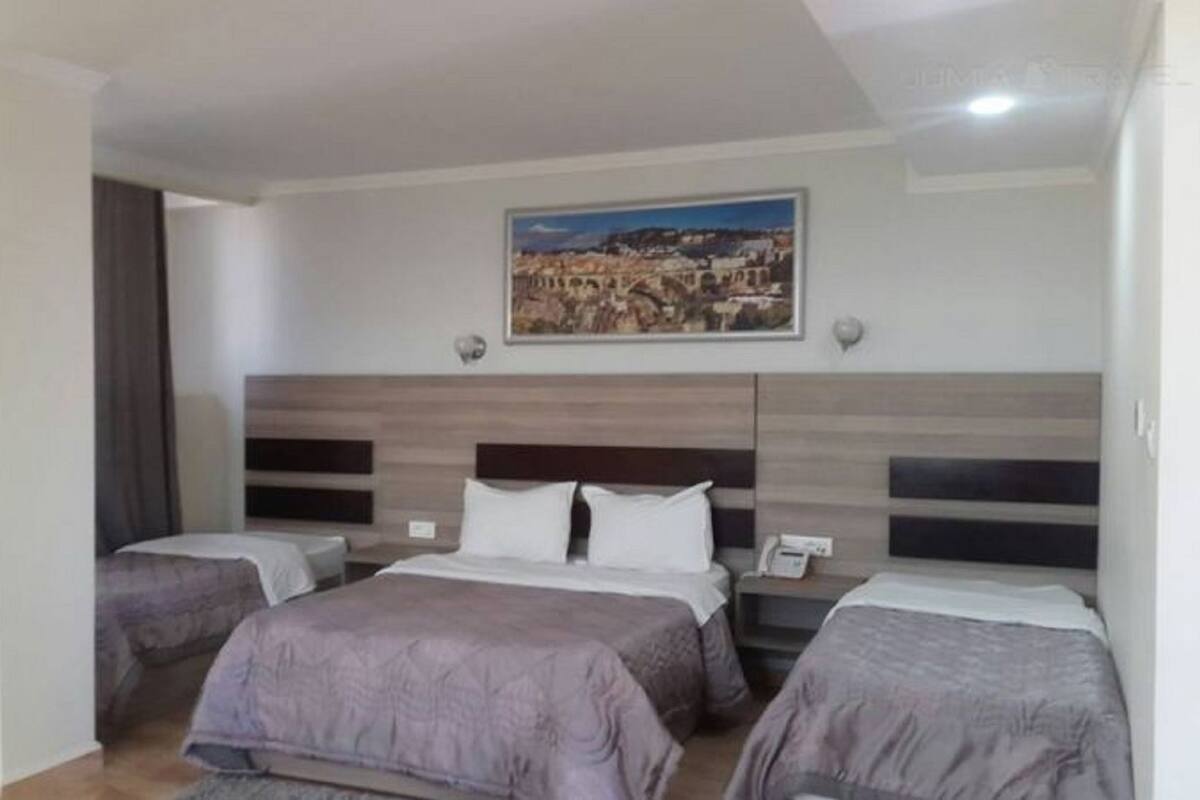 A hotel room with two beds, a large window, and a cityscape painting on the wall.