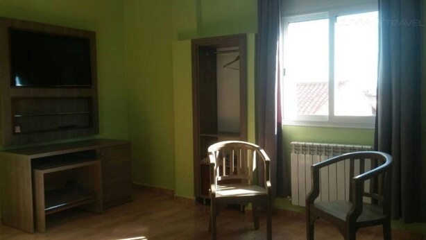 Una habitación con un armario de madera, televisión, una silla y una ventana con cortinas.