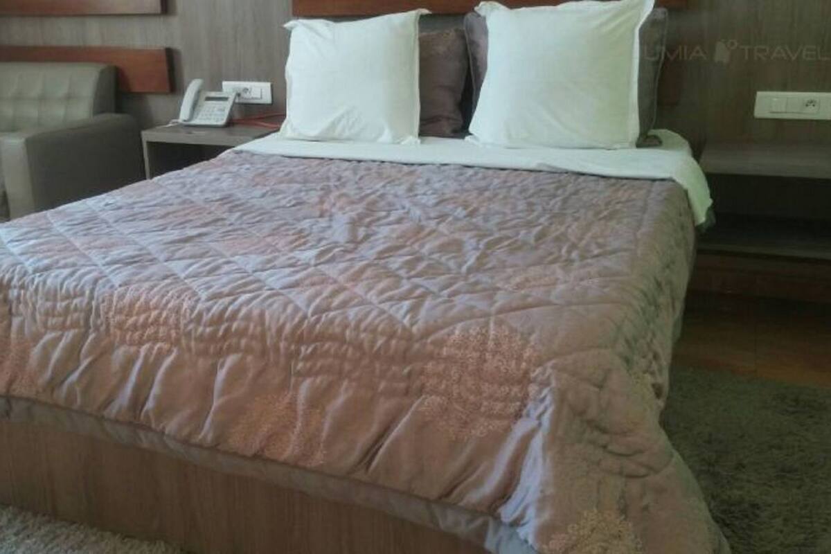 A neatly made bed with a patterned bedspread, a bedside table with a lamp, and a chair in a hotel room.