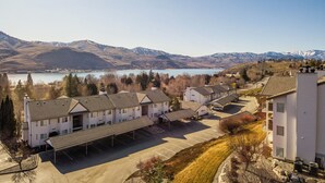 A residential area with a row of white buildings, a parking lot, and a lake with mountains in the background. - Park Pointe C204 - Community Pool/Hot tub (Chelan)