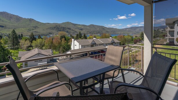 A balcony with a table and chairs, overlooking a scenic view of mountains and a lake. - Park Pointe C204 - Community Pool/Hot tub (Chelan)