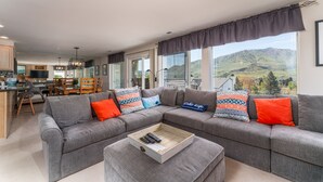 A modern living room with a grey sectional sofa, a wooden coffee table, and a view of a mountainous landscape through large windows. - Park Pointe C204 - Community Pool/Hot tub (Chelan)