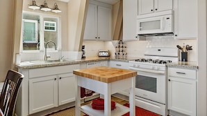 A kitchen with white cabinets, a wooden table, a sink, a stove, and a toaster.