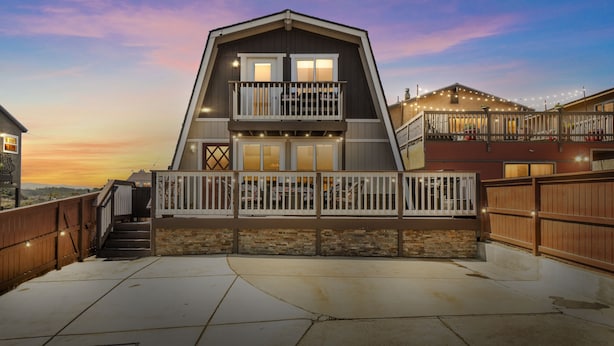 A two-story house with a balcony, a stone foundation, and a wooden fence.