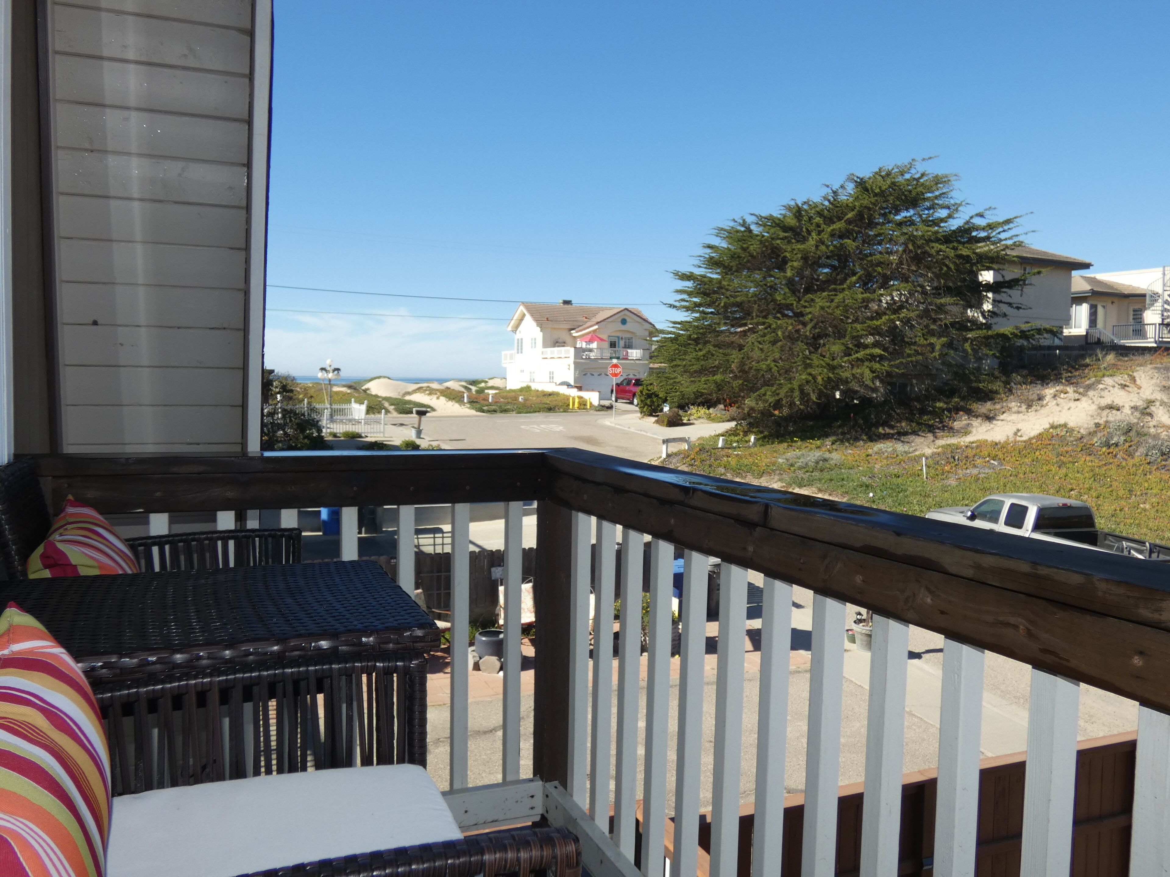 A balcony with a wicker chair and a striped pillow, overlooking a residential street with houses and a stop sign.