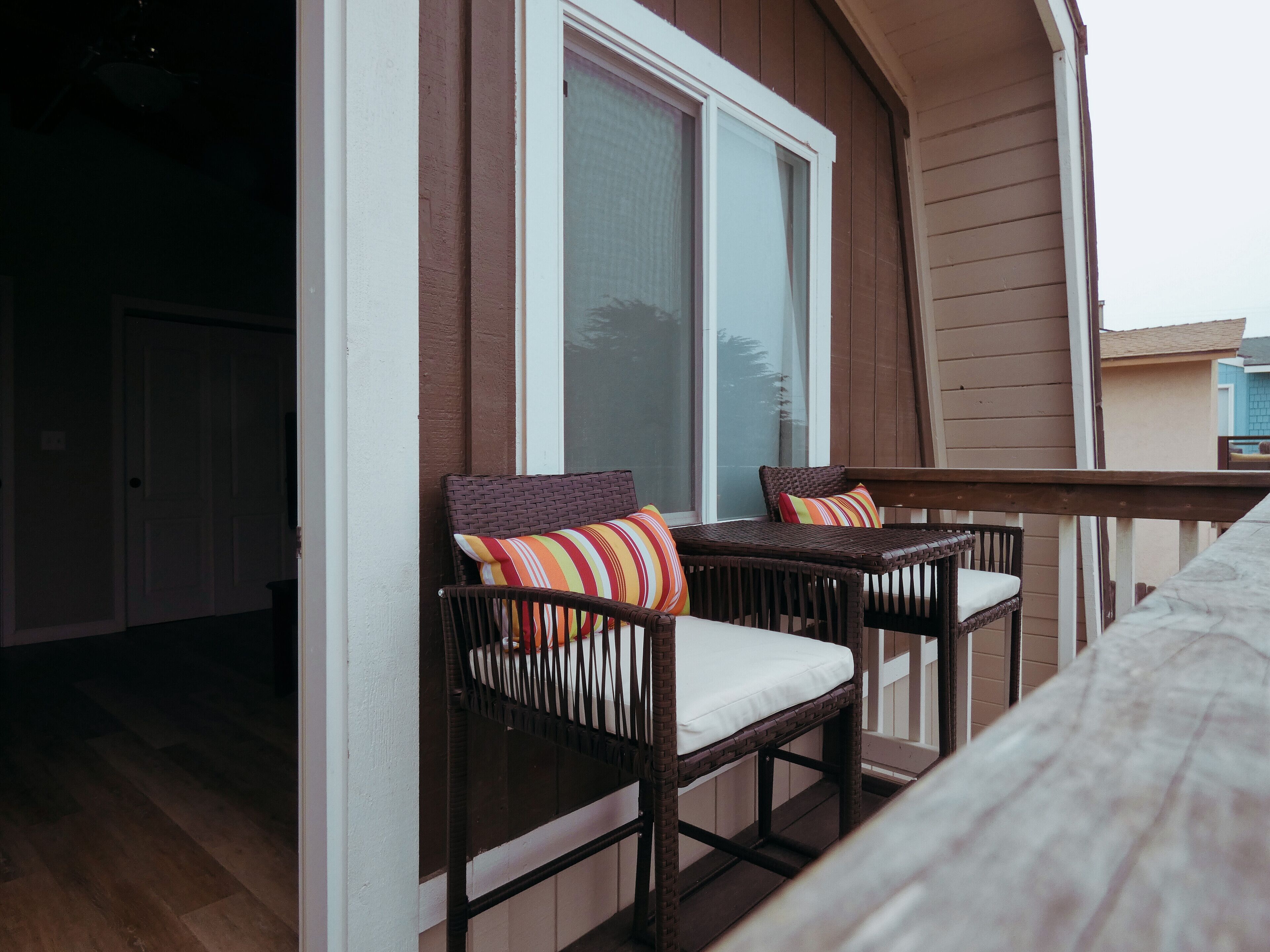 Un balcon avec deux fauteuils en osier, chacun agrémenté d’un coussin et d’un oreiller à rayures.