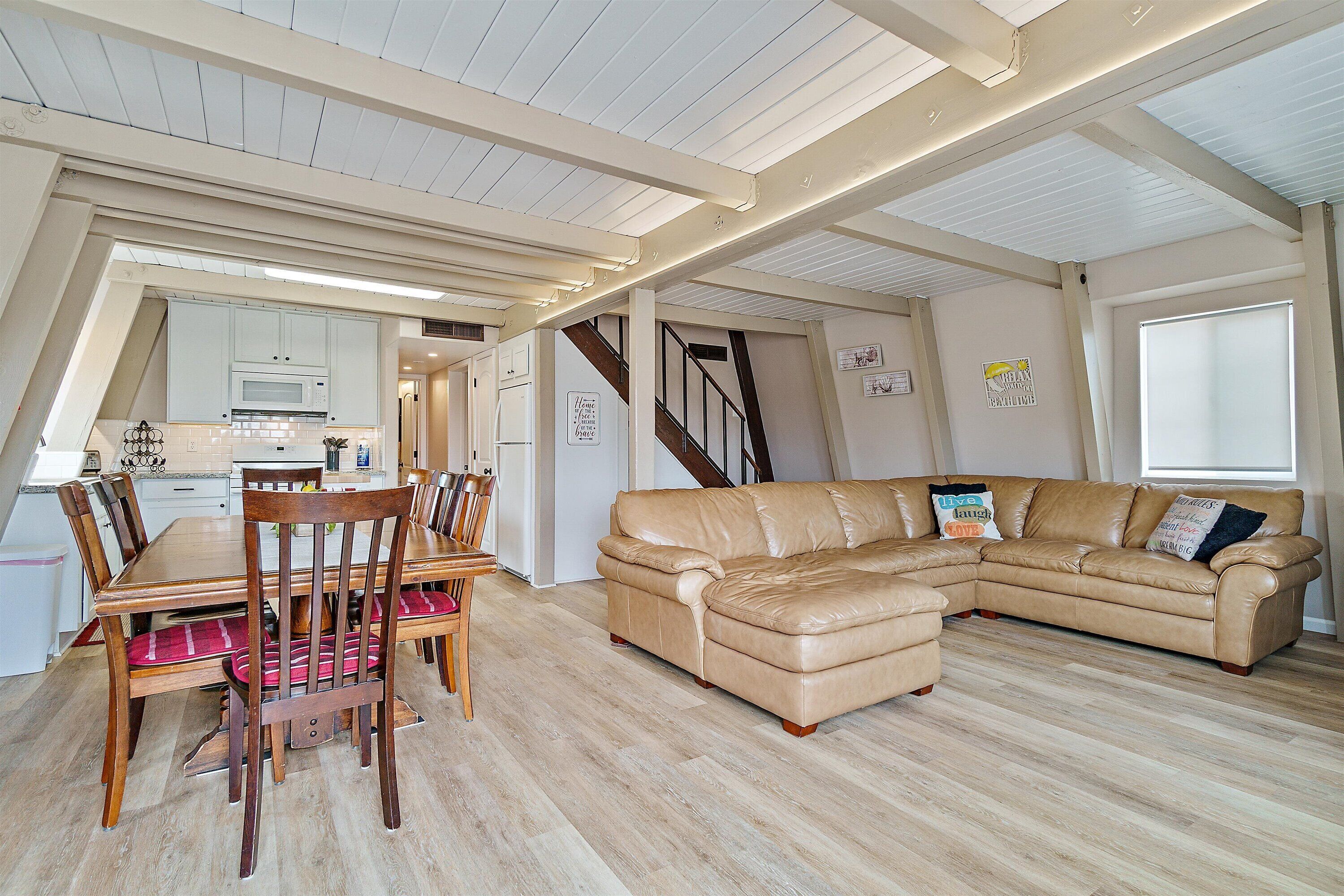 A spacious living area with a large L-shaped leather sofa, wooden dining table with chairs, and a kitchen in the background.