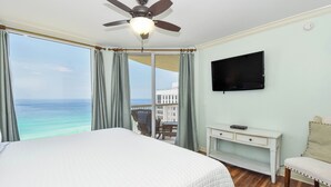 Habitación de hotel con cama, ventilador de techo, televisión, escritorio y vistas al océano.