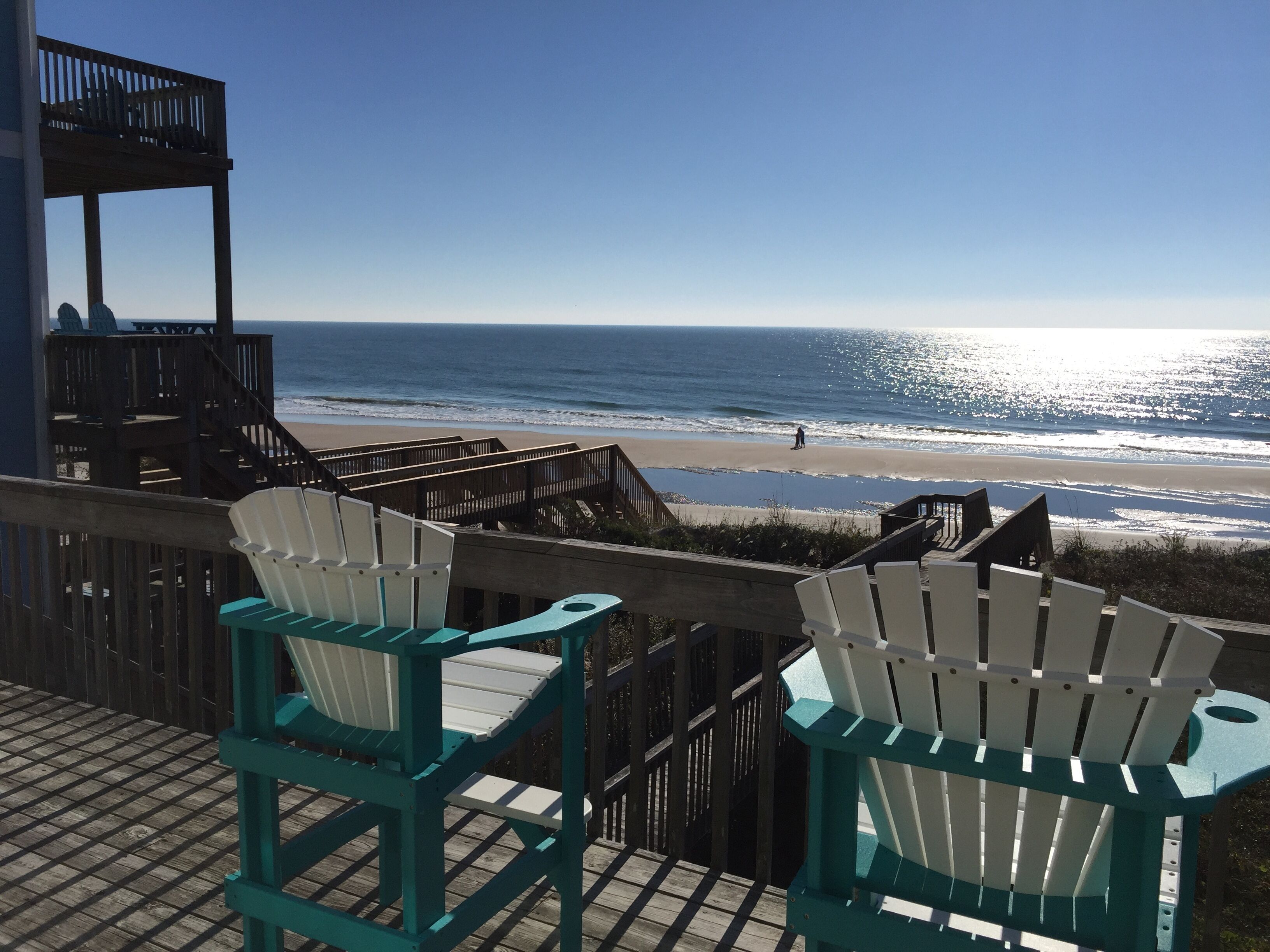 Une terrasse en bois avec deux fauteuils Adirondack donnant sur une plage.